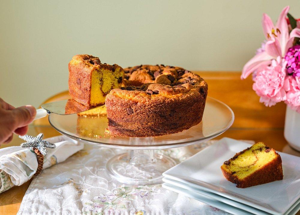 Bundt cake on a glass stand, slice being served, pink flowers nearby.