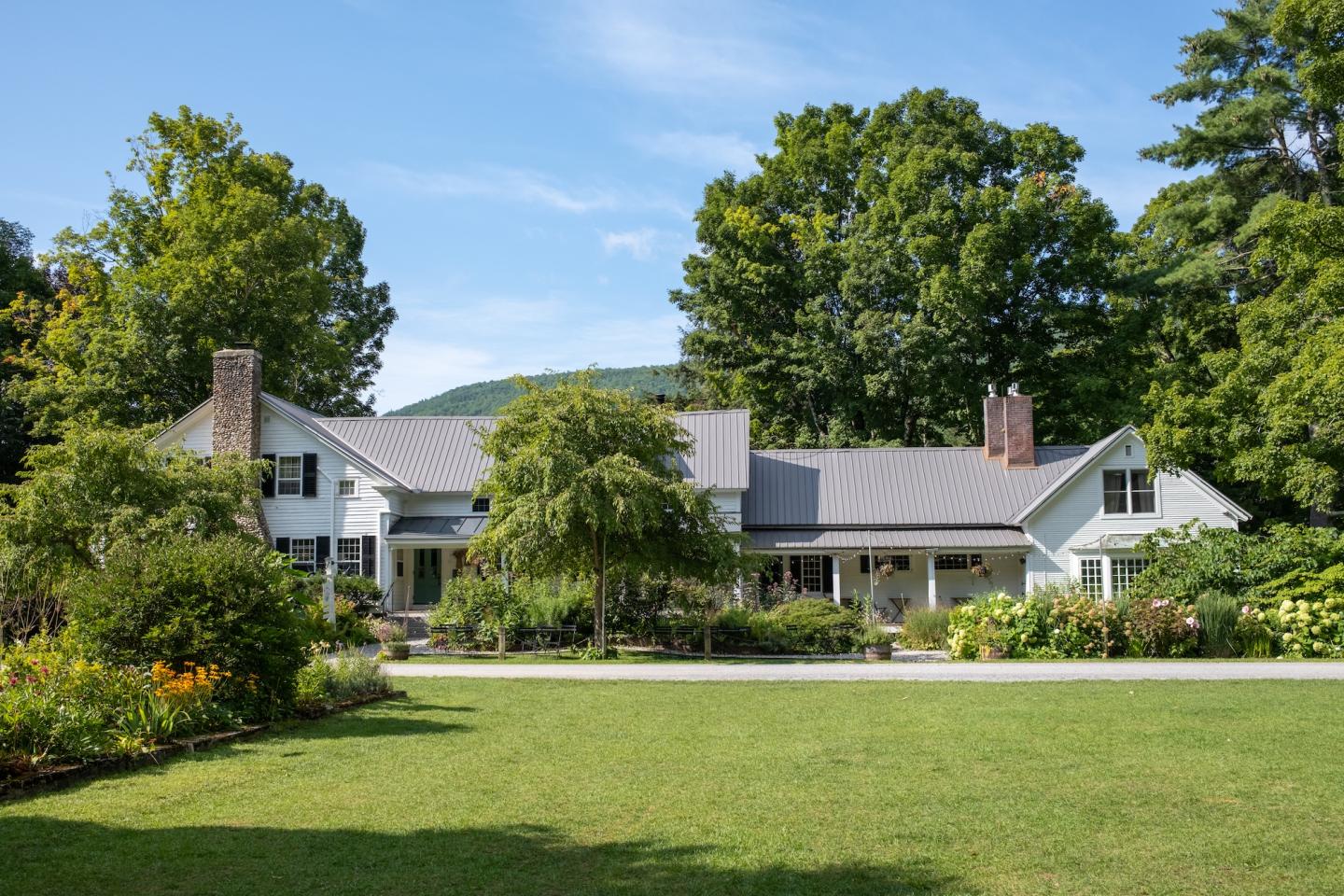 Large house with a gray roof, surrounded by lush greenery and gardens.