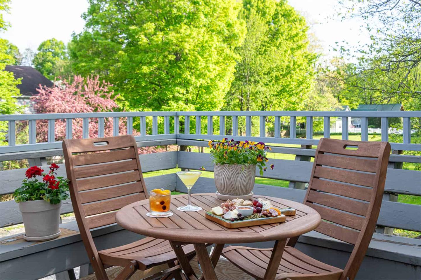Wooden patio set on a balcony with plants and a view of lush trees.