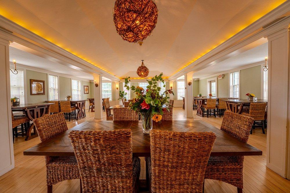 Dining room with wicker chairs and a floral centerpiece. Warm lighting and wood floors.