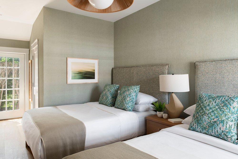 Two beds in a bright room with green walls and a lamp on a side table.