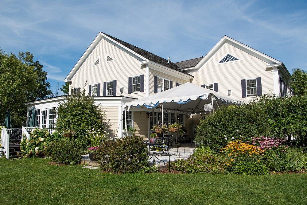 Large white house with a garden and awning on a sunny day.