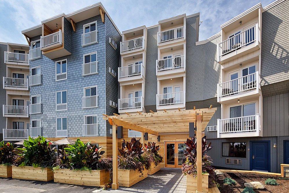 Four-story apartment building with a central wooden entrance and planters.