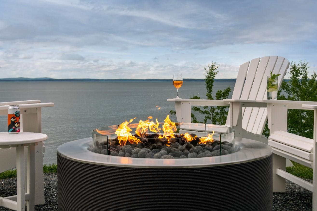 Fire pit on a patio with Adirondack chairs and lake view.