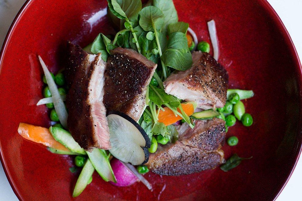 Grilled meat with fresh vegetables on a red plate.