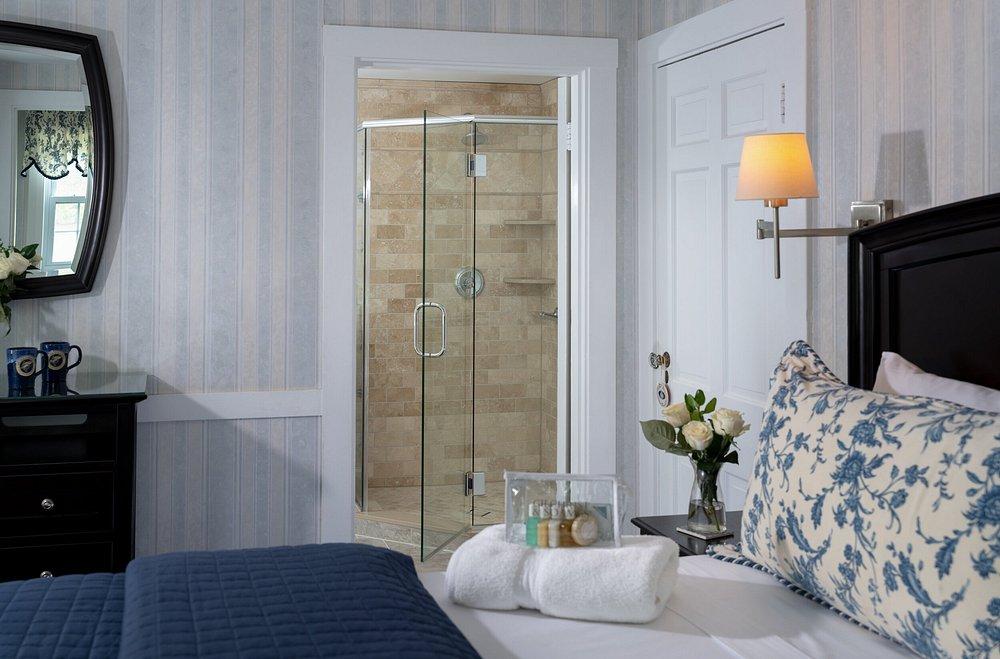 Stylish bedroom with floral pillow, towels, and en suite glass shower.