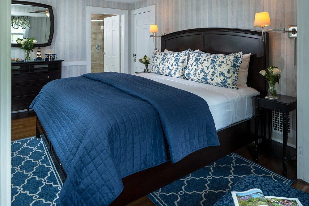 Cozy bedroom with blue bedding and floral pillows, soft lighting, and wooden furniture.