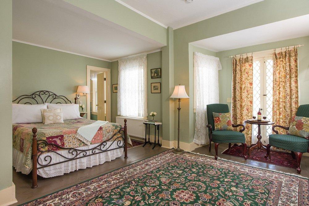 Elegant bedroom with green walls, ornate bed, armchairs, and floral curtains.