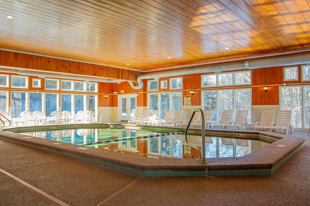 Indoor pool with wooden ceiling, surrounded by lounge chairs and large windows.