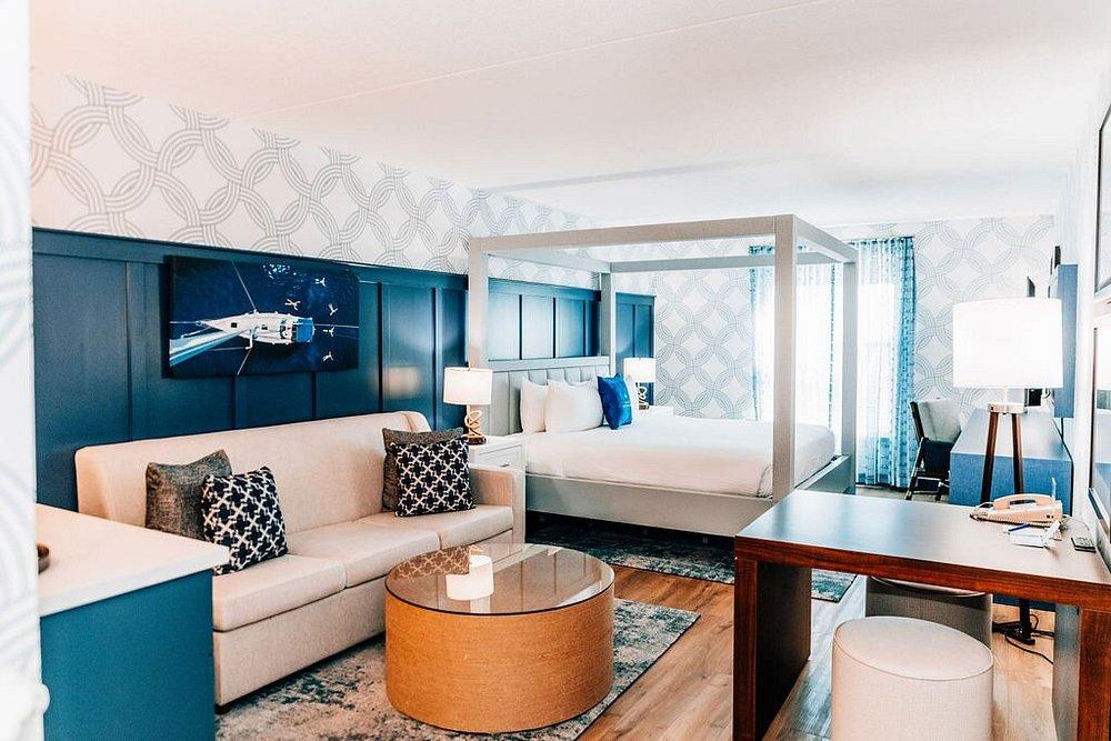 Modern hotel room with bed, sofa, and desk, decorated in blue and white tones.