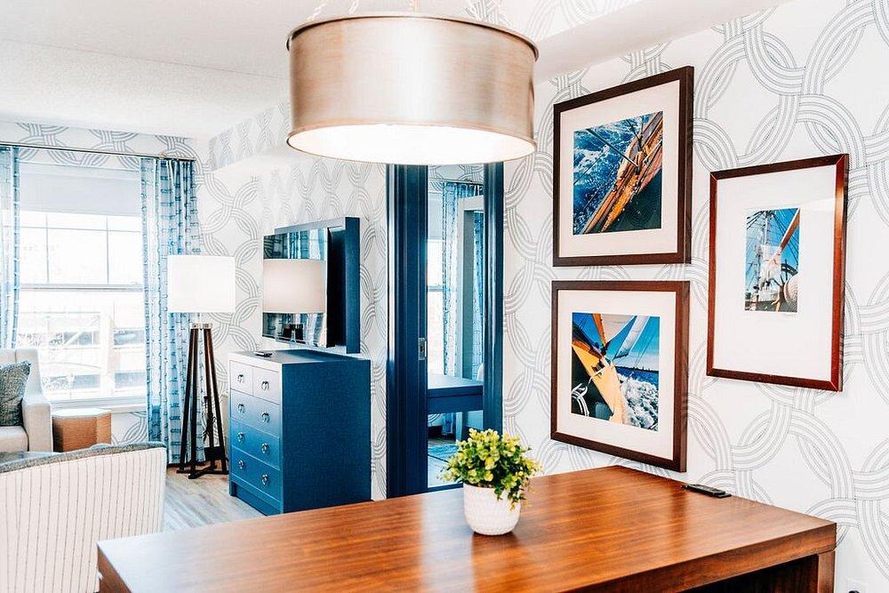 Bright room with framed photos, wooden table, potted plant, and large ceiling light.
