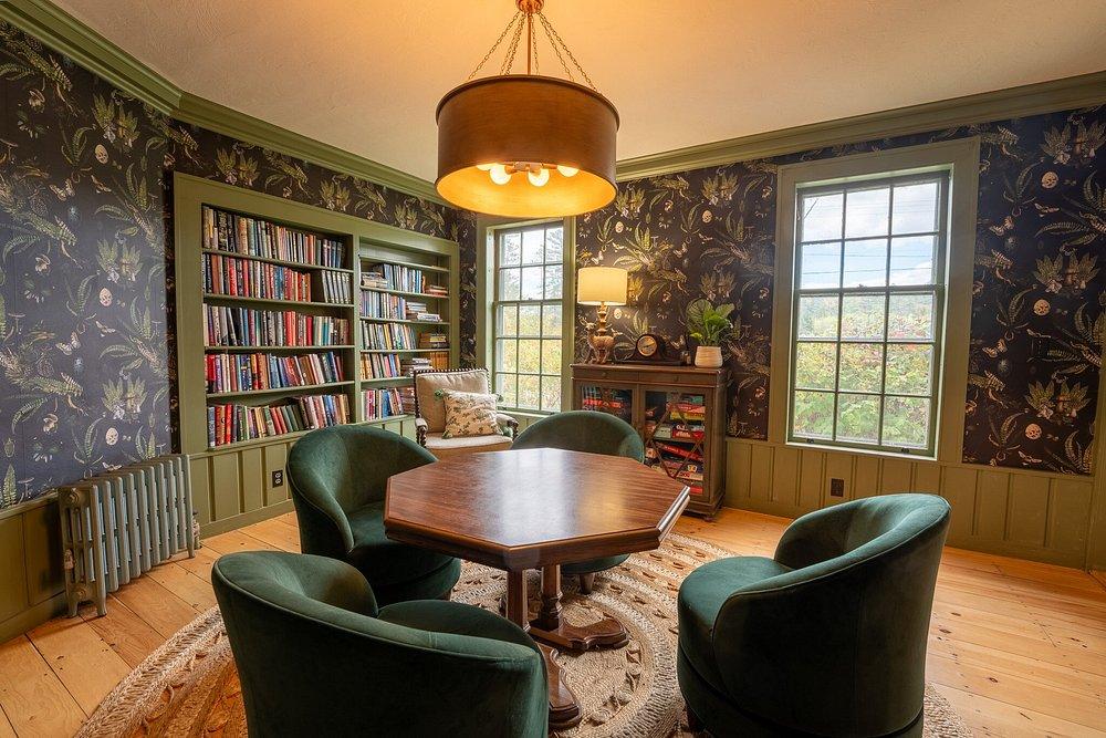 Cozy study with green chairs, wooden table, bookshelves, and large windows.