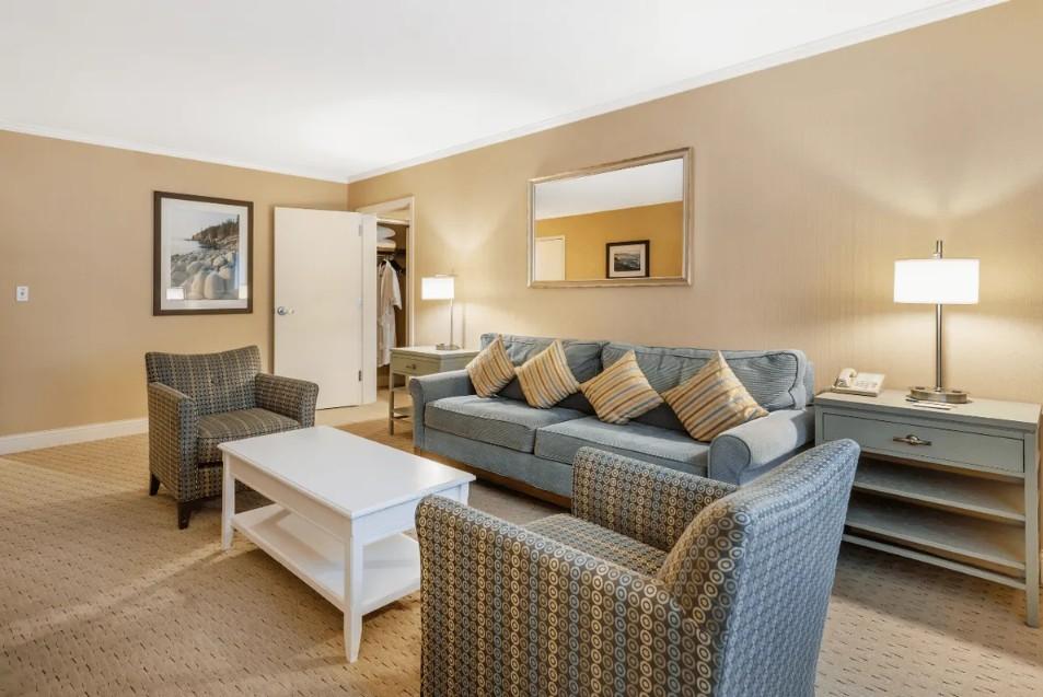 Cozy living room with blue sofa, armchairs, and lamps. Beige walls and carpet.