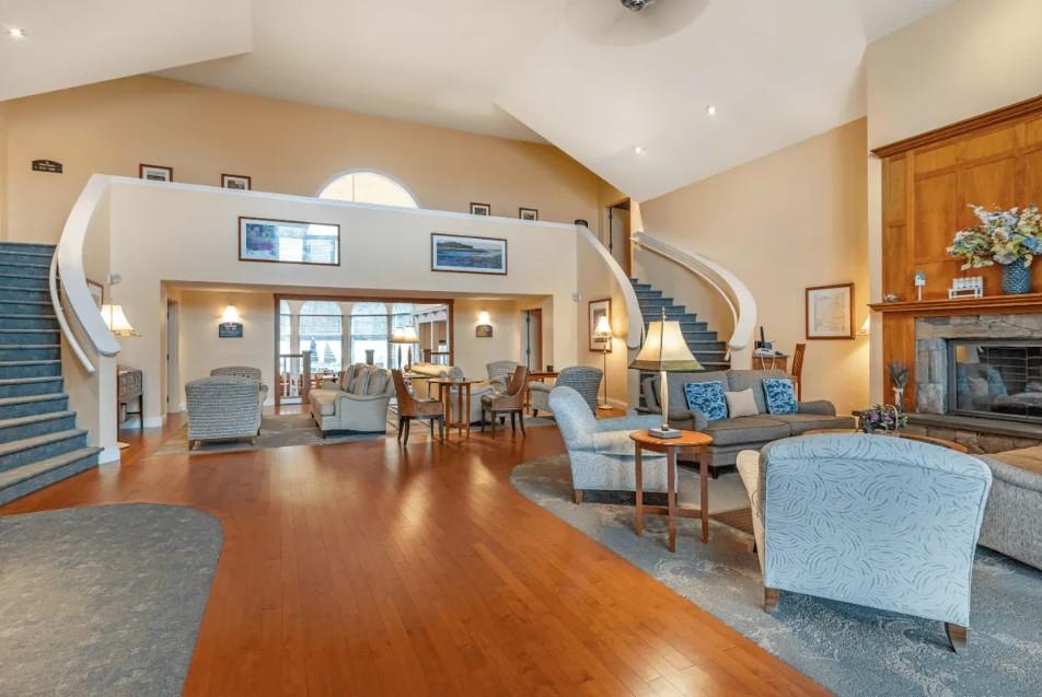 Elegant lobby with curved staircase, plush seating, large fireplace, and wooden flooring.