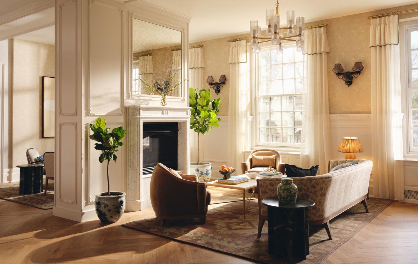 Sunlit elegant living room with fireplace, chandelier, sofas, and plants.