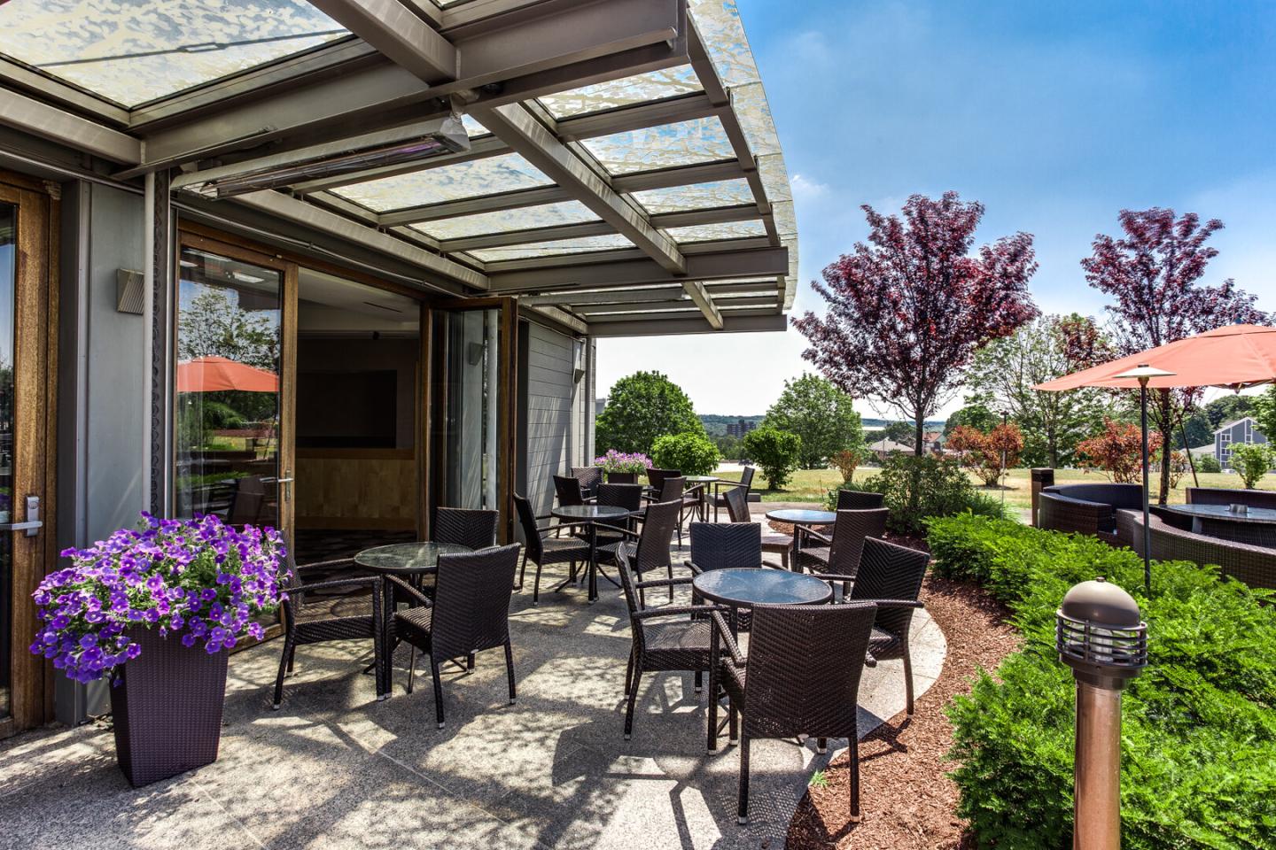 Outdoor patio with tables, chairs, and purple flowers under a clear sky.