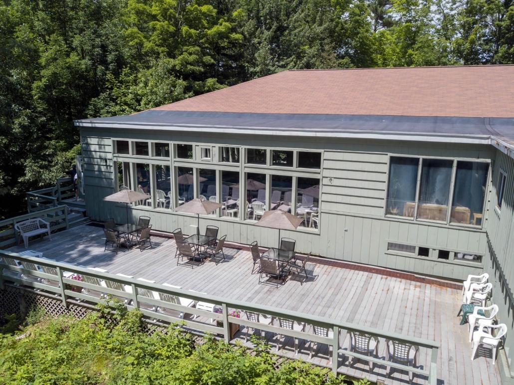 Large deck with tables and umbrellas outside a house surrounded by trees.