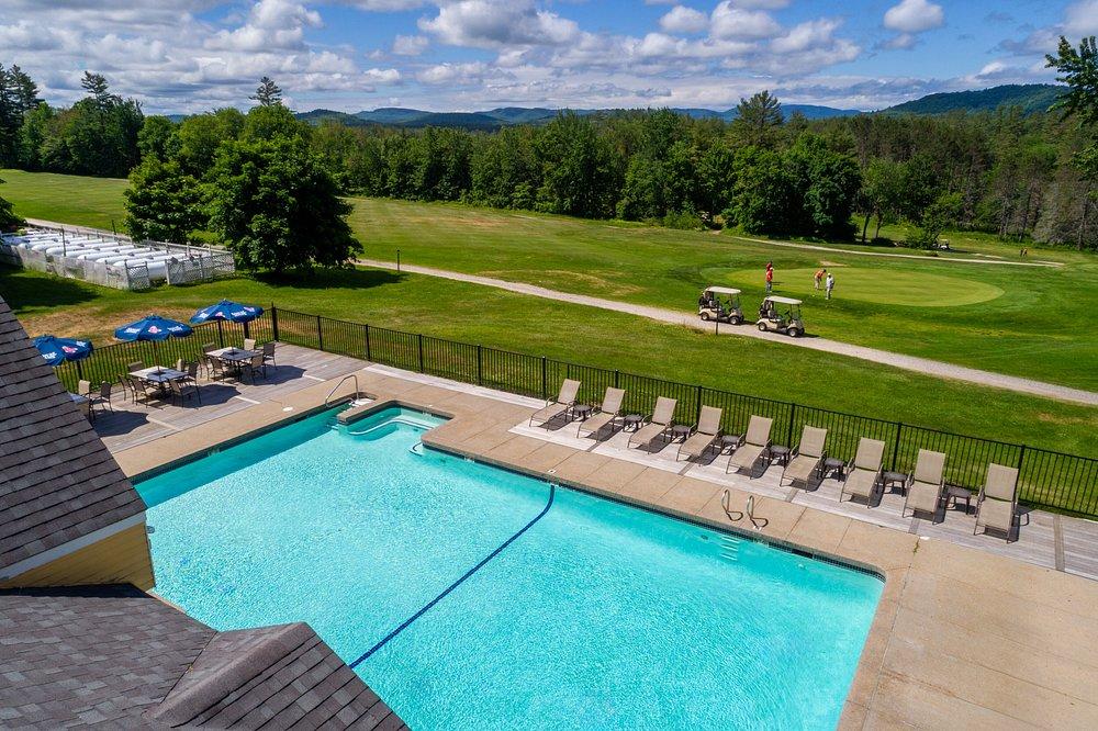 Swimming pool with lounge chairs, golf course view, under a partly cloudy sky.