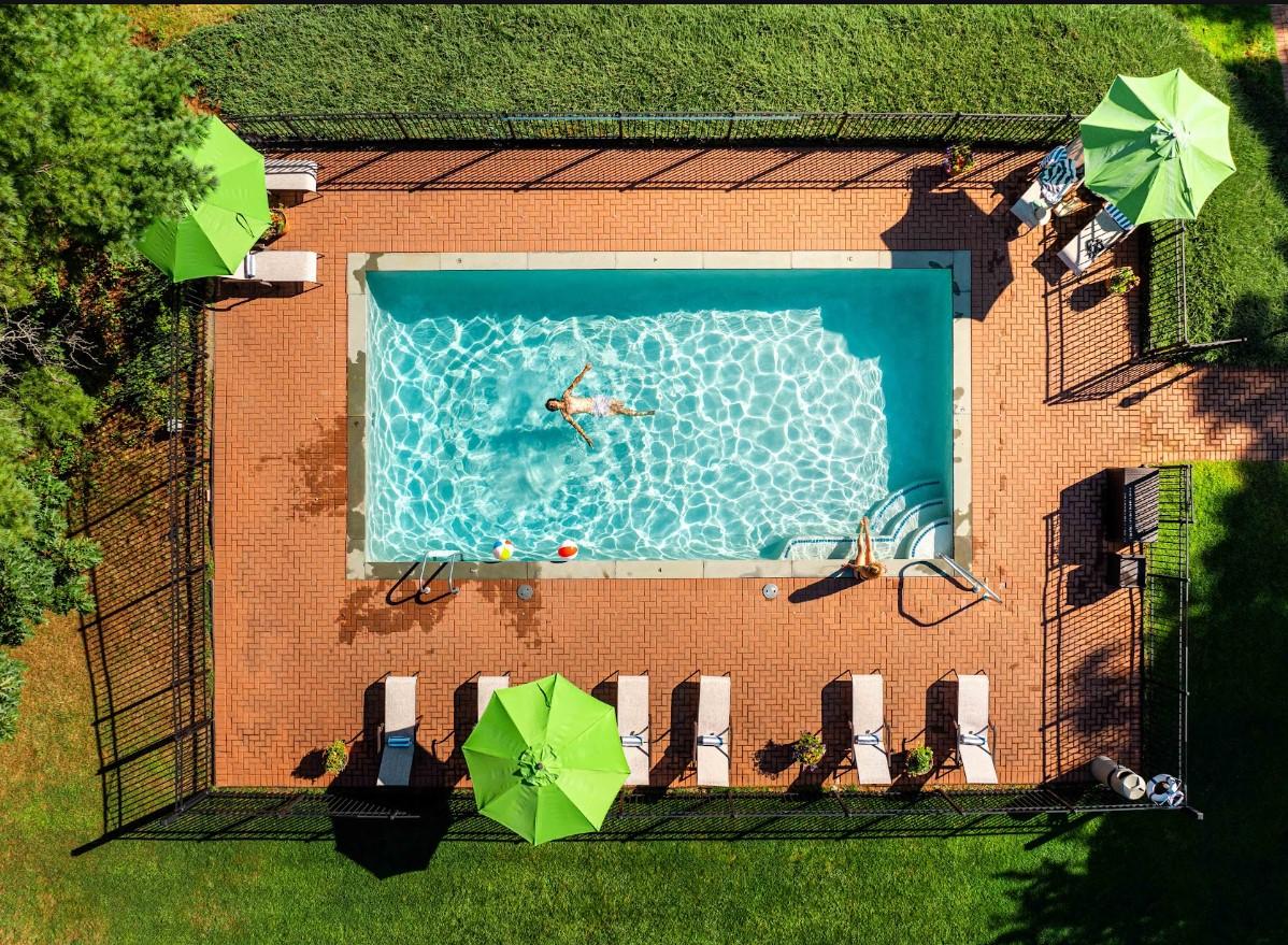 Aerial view of a fenced swimming pool with loungers and green umbrellas.