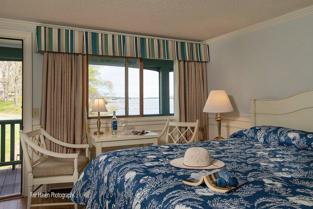 Cozy bedroom with blue floral bedding, a hat on the bed, and a view of the water through the window.