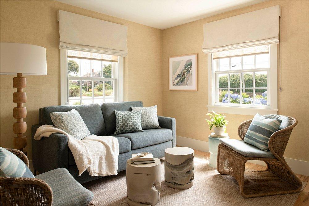 Cozy living room with a gray sofa, wicker chairs, and sunlit windows.