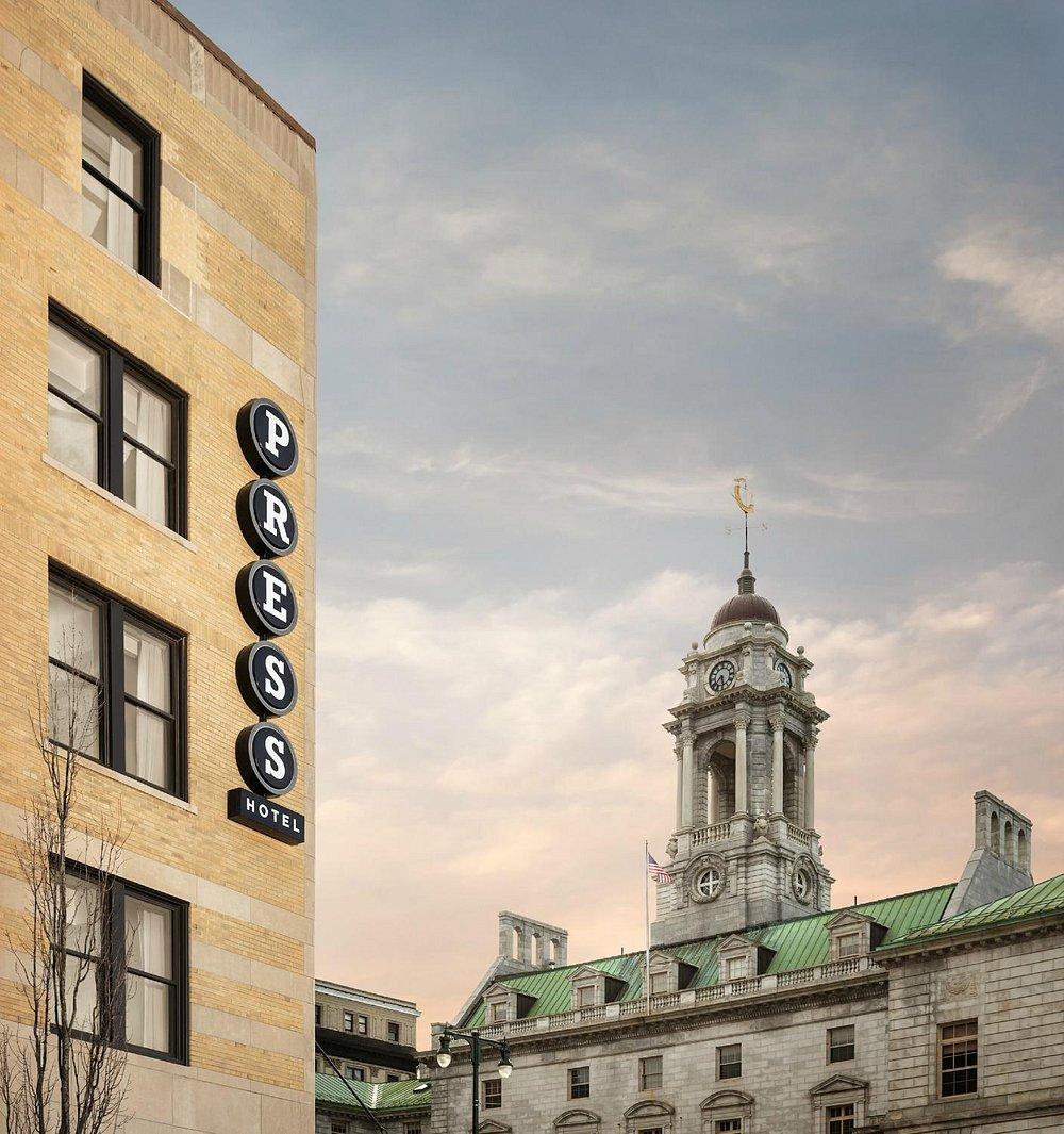 Press Hotel sign with historic building and cloudy sky.
