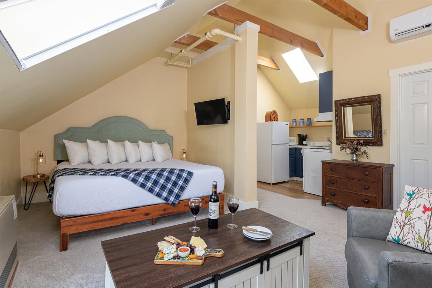 Cozy attic bedroom with skylights, bed, small kitchen, and a table with wine and snacks.