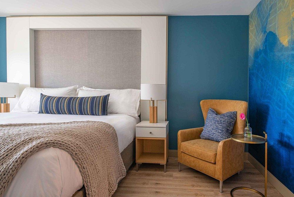 Stylish hotel room with a large bed, blue accent wall, and cozy armchair.