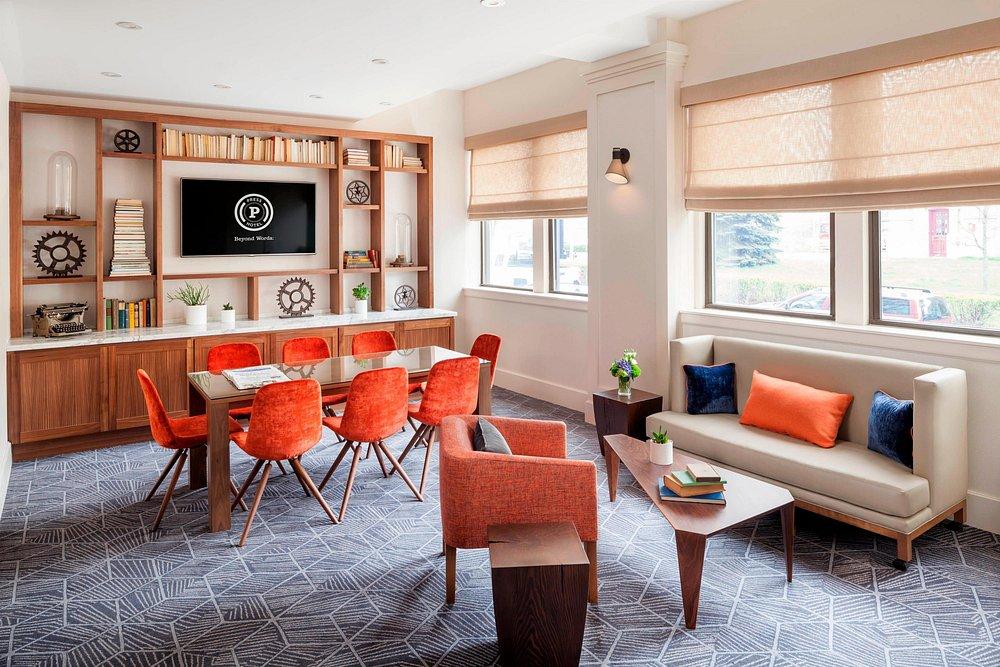 Modern meeting room with red chairs, sofa, and a TV on wooden shelves.