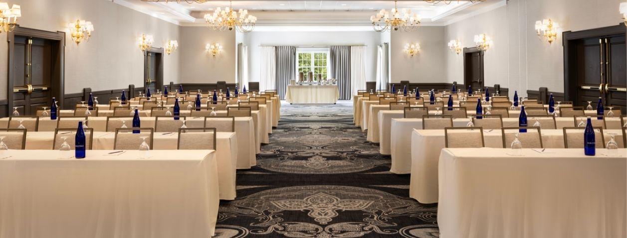 Elegant ballroom set for a conference with rows of beige-covered chairs.