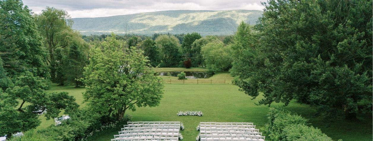 Lush garden aisle with white chairs facing a distant ceremony spot.