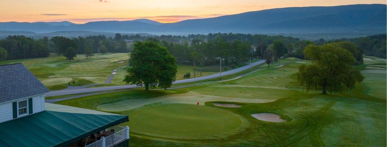 Golf course at sunset with rolling fairways, trees, and distant hills