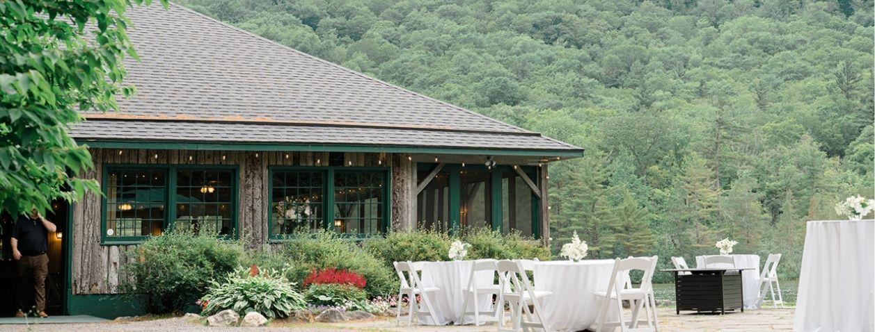 Outdoor patio with white tables and chairs beside a rustic wooden building.