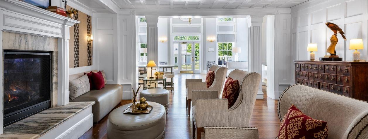 Bright living room with fireplace, white sofas, armchairs, and large windows.