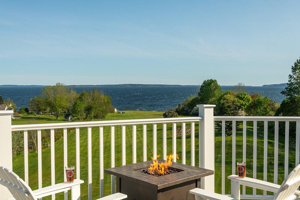 Patio fire table overlooking a blue lake and tree-lined shore.