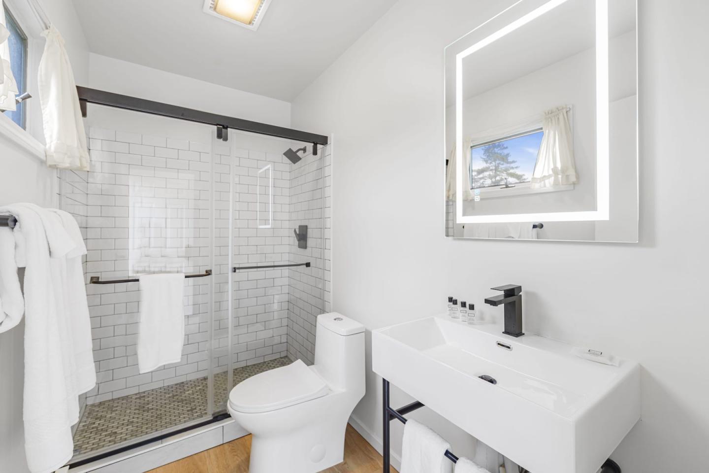 Bright modern bathroom with walk-in tiled shower, white vanity, and toilet.