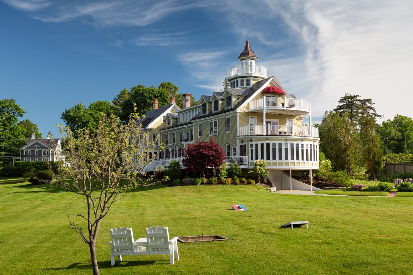 Large white Victorian house with a tower overlooking a sunny green lawn.