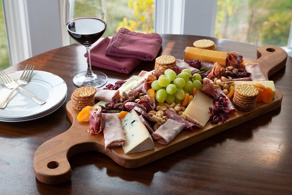 Charcuterie board with cheeses, grapes, meats, crackers, and wine on a wooden table.