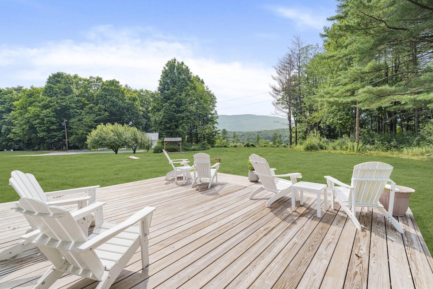 Wooden deck with white Adirondack chairs overlooking a green lawn and trees.