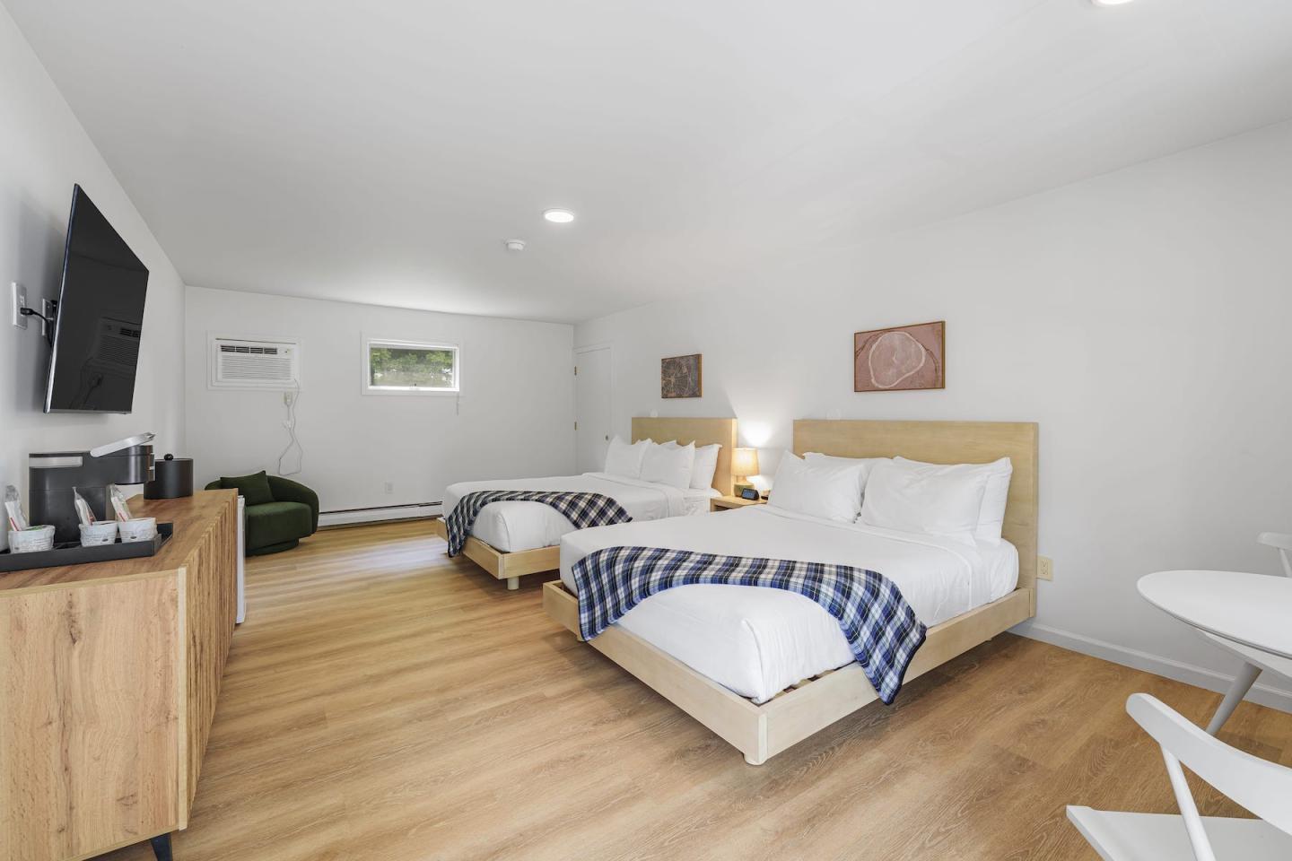 Bright minimalist bedroom with two beds, wooden floor, and blue checkered blankets.
