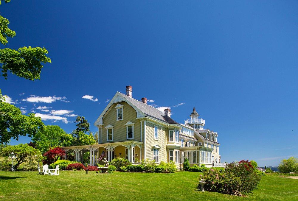 Large Victorian mansion with ornate white trim on a sunny green lawn.