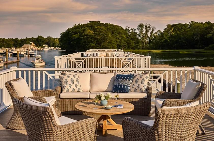 Wicker patio seating around a fire table overlooking a marina at sunset.