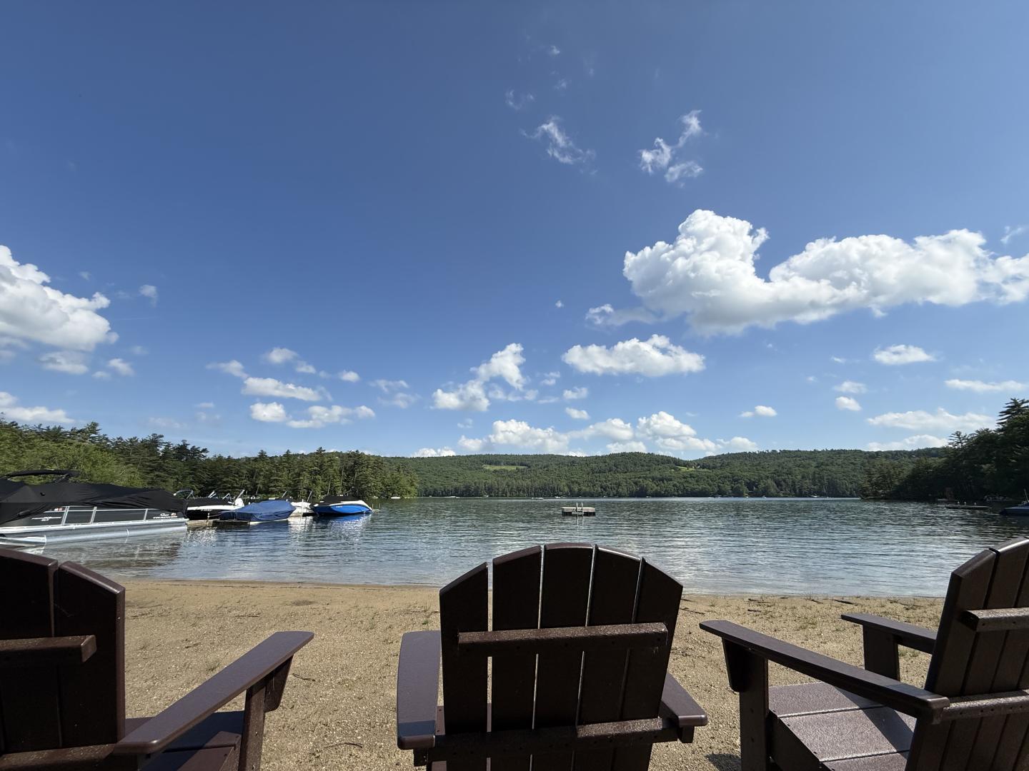 Lake view from a dock with Adirondack chairs under a blue sky.