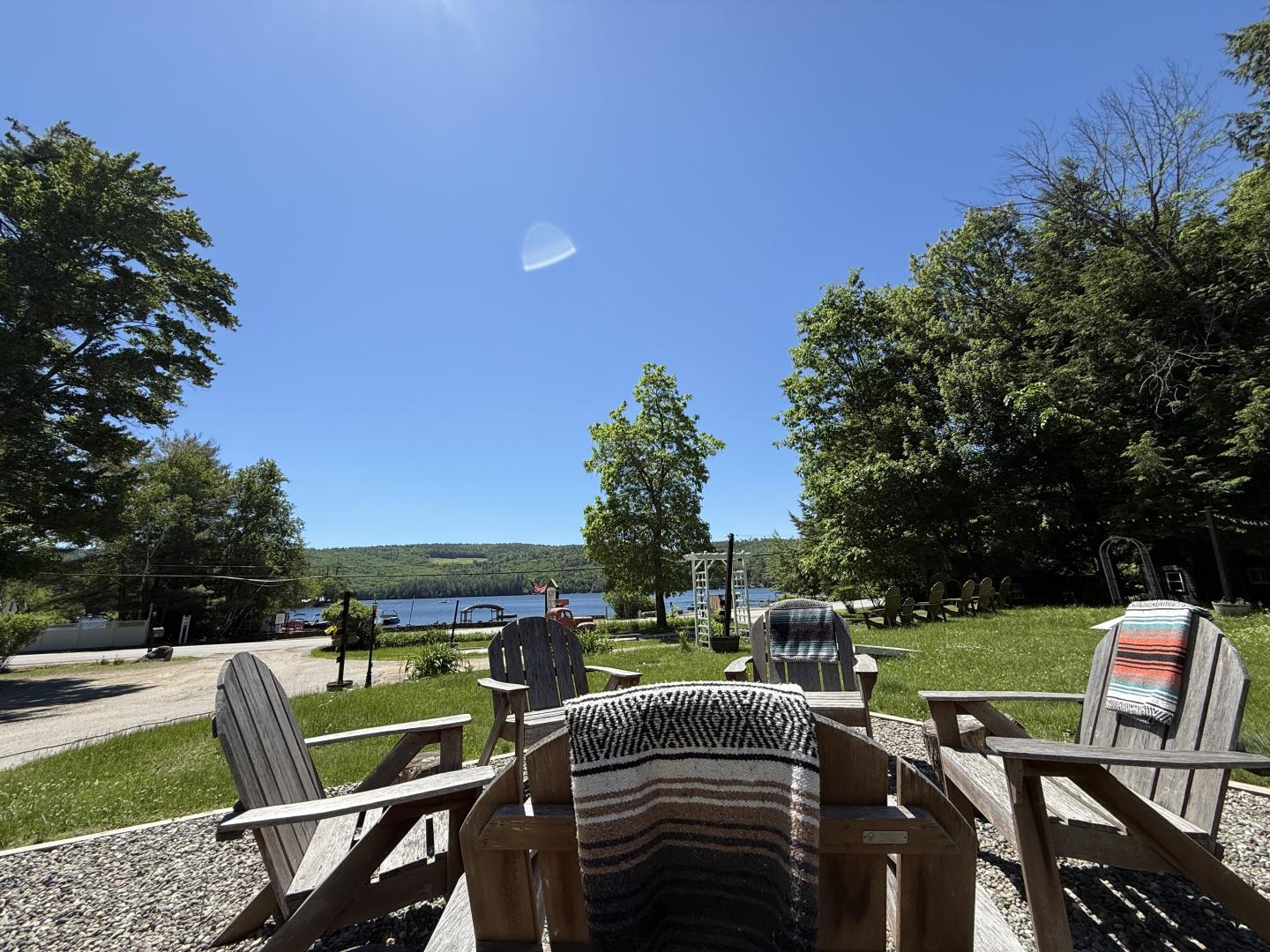 Patio chairs and tables overlooking a sunny lake, framed by trees.