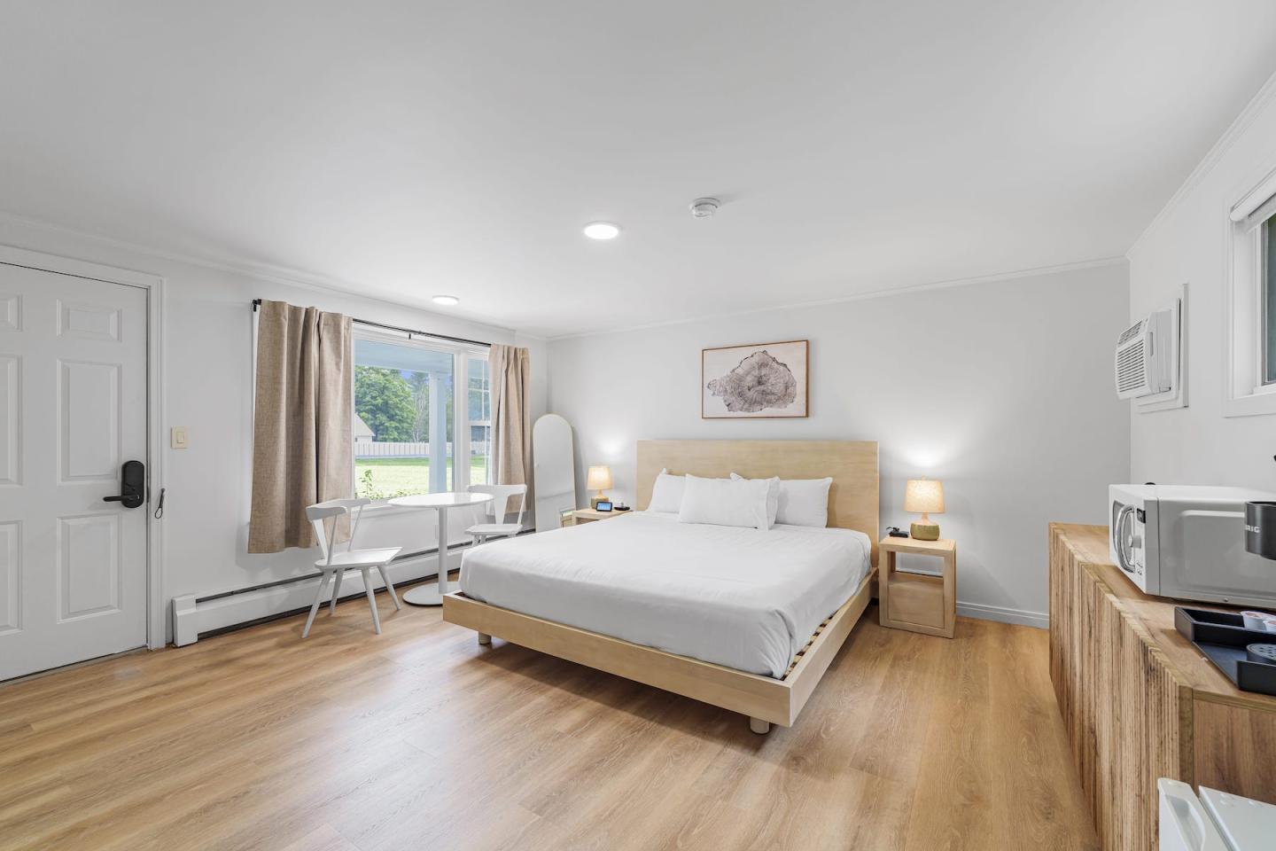 Bright modern bedroom with white bed, wooden floor, desk, and balcony doors.