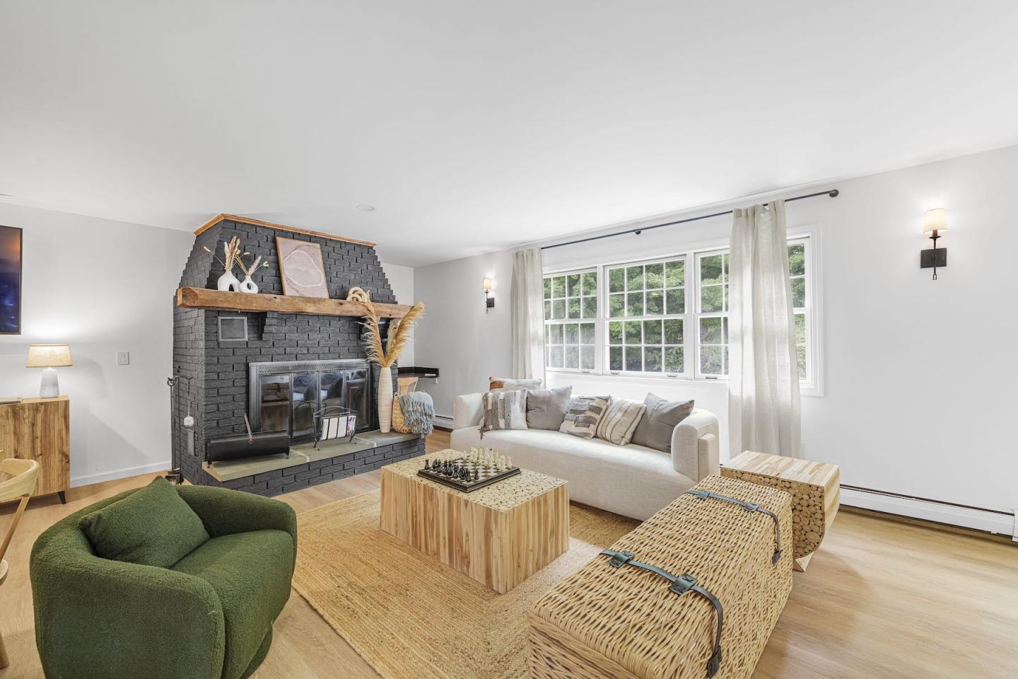 Bright living room with green armchairs, patterned sofa, fireplace, and large windows.