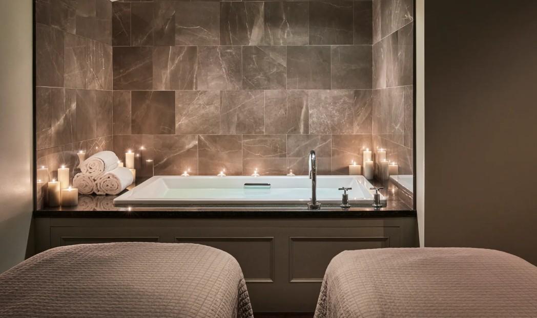 Two twin beds face a bathroom vanity with a large marble mirror and warm candlelight.