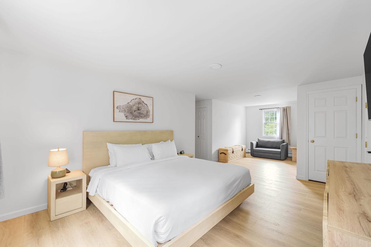 Bright minimalist bedroom with white bed, wood floors, and a small desk.