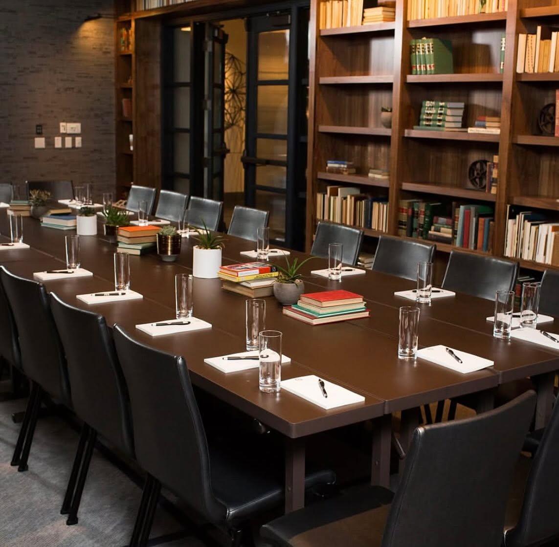Elegant dining table set with black chairs, place settings, and bookshelves.