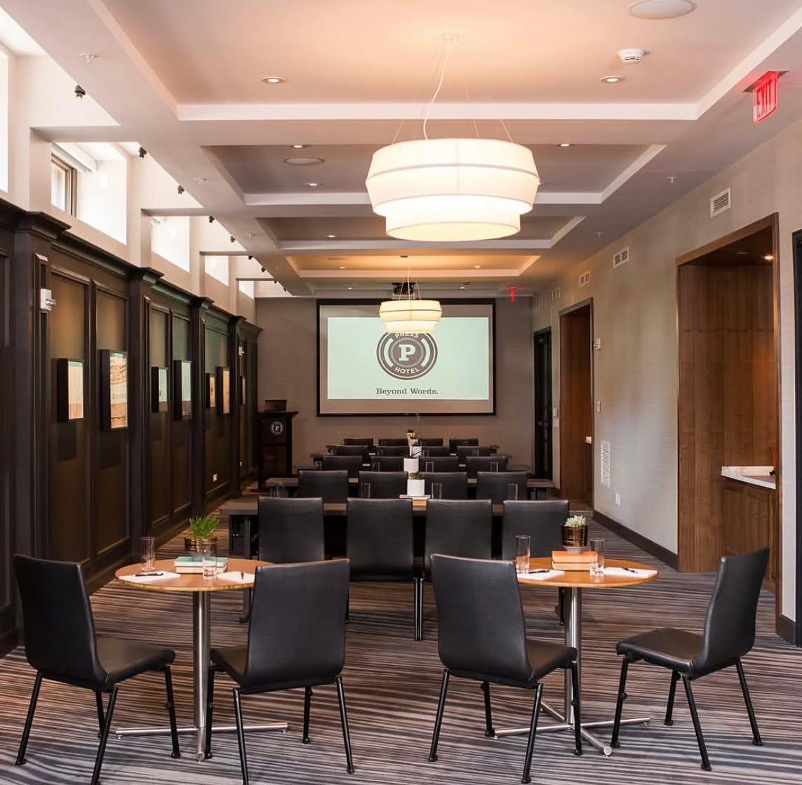 Modern hotel lounge with black chairs, round tables, and a projection screen.